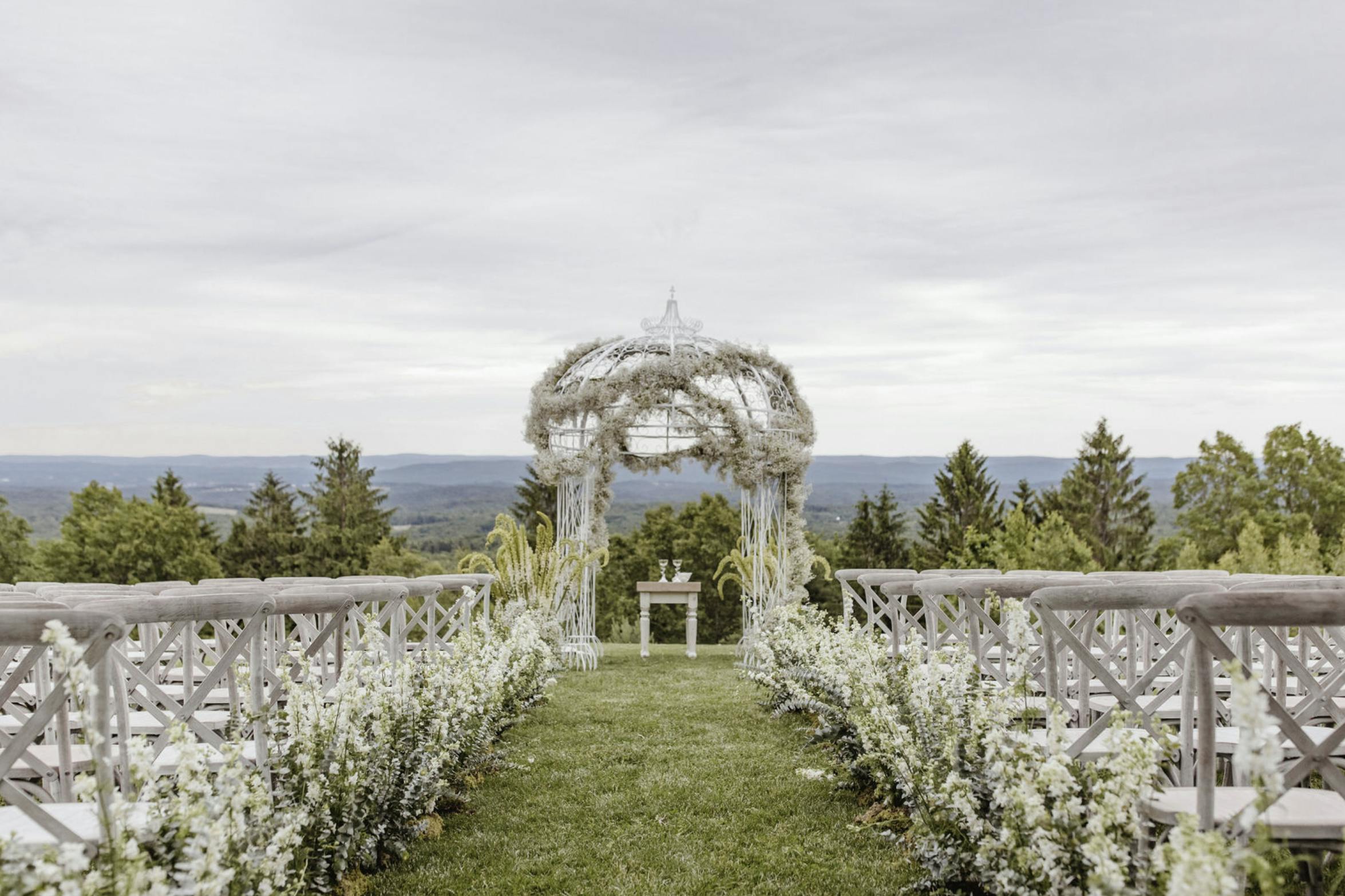 A White Filigree Wedding Arbor Wound with a Garland of Baby’s Breath | PartySlate