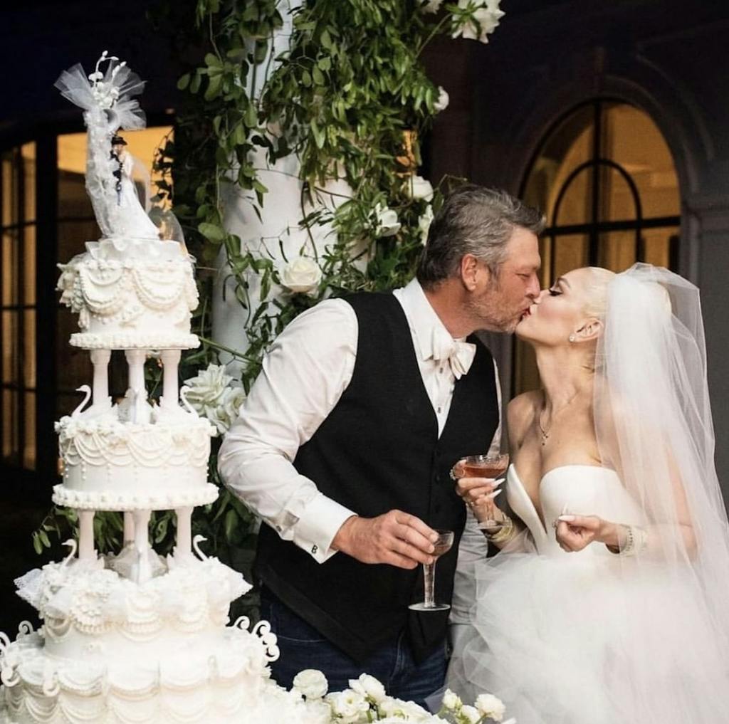 Gwen Stefani and Blake Shelton Kiss in front of Tiered White Wedding Cake | PartySlate