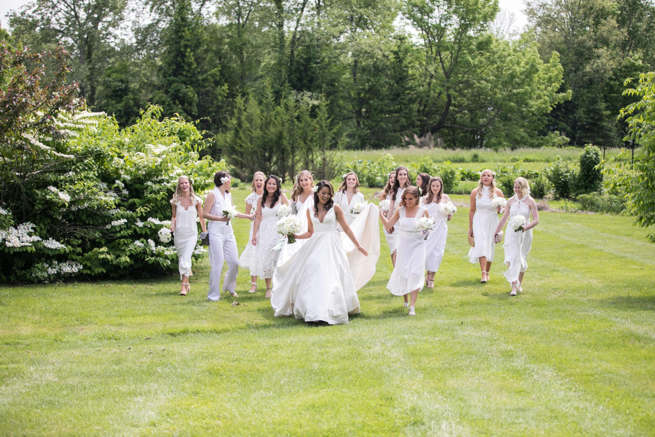 Bridal party in all white running through greenery field | PartySlate
