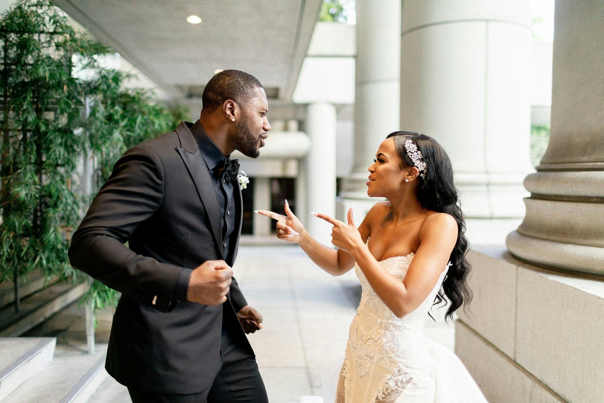 Bride and groom having a silly moment, bride doing finger guns at groom in all black suit | PartySlate