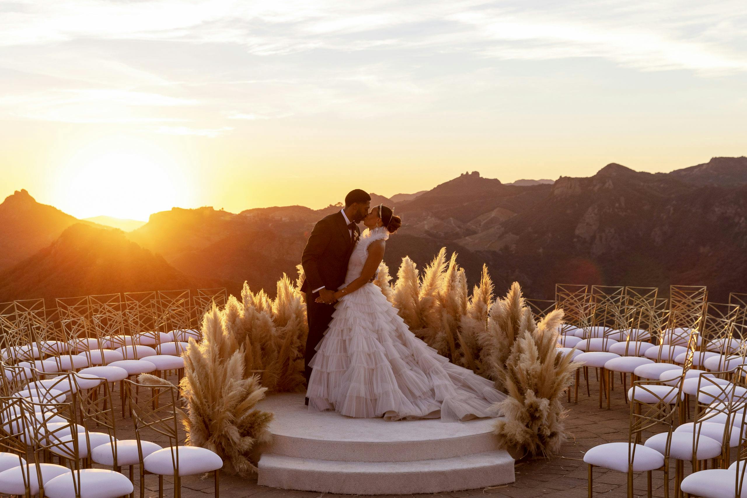 Bride and groom kissing with mountain background and sun setting | PartySlate