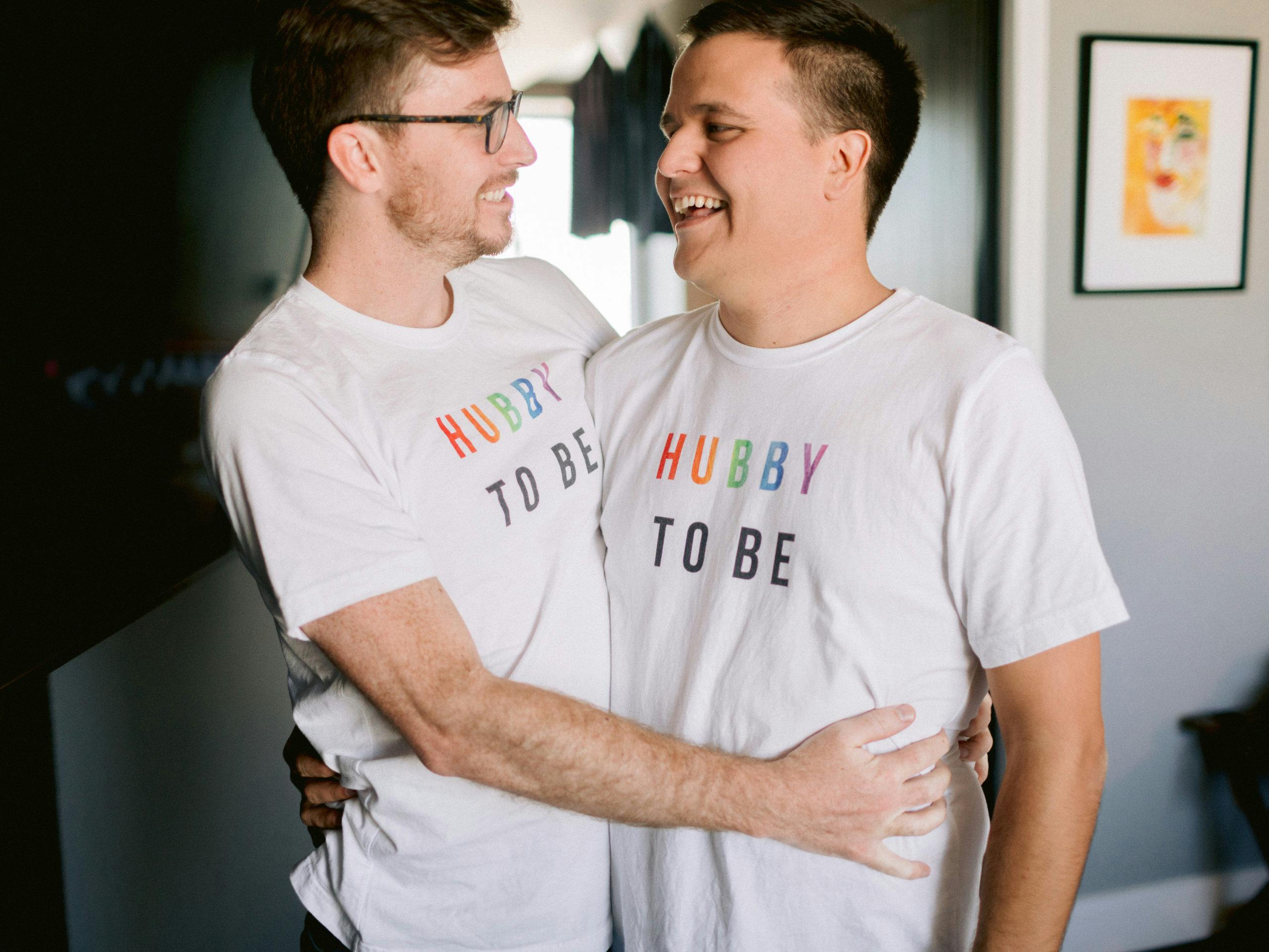 grooms in matching “Hubby To Be” t-shirts embrace | PartySlate
