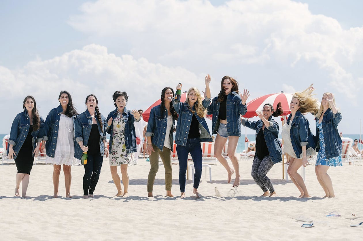 Bridal party jumping on the beach in matching jean jackets