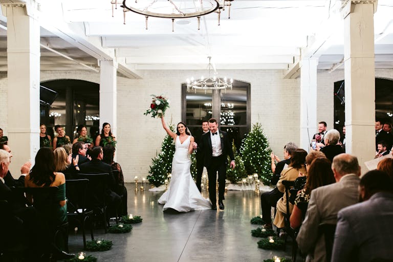 Happy couple at the altar rejoicing at elegant loft wedding with string-lit evergreen trees in backdrop at Company 251 in Aurora, IL | PartySlate