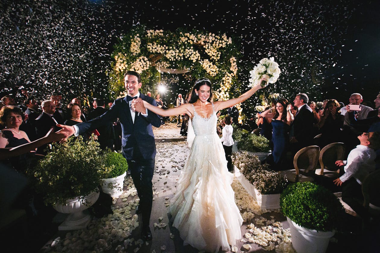 Bride and groom walking down aisle with joy after night wedding ceremony and twinkling lights | PartySlate