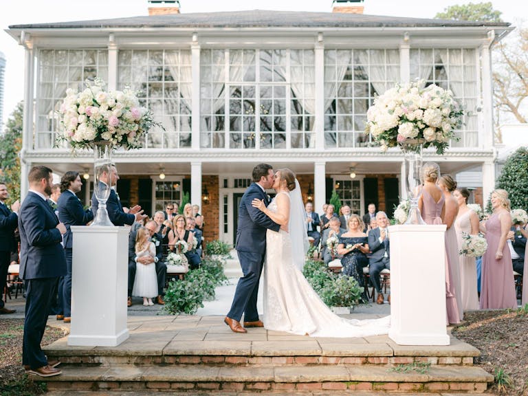 Bride and Groom Kiss at Outdoor Wedding Reception Set Against The Estate by Legendary Events in Atlanta, GA | PartySlate