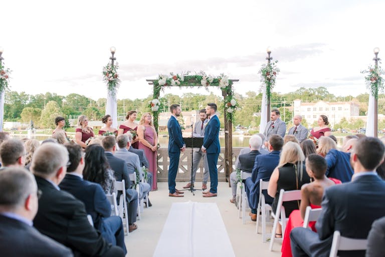 Two grooms sharing vows at a peaceful countryside ceremony at Hotel Baker in St. Charles, IL | PartySlate