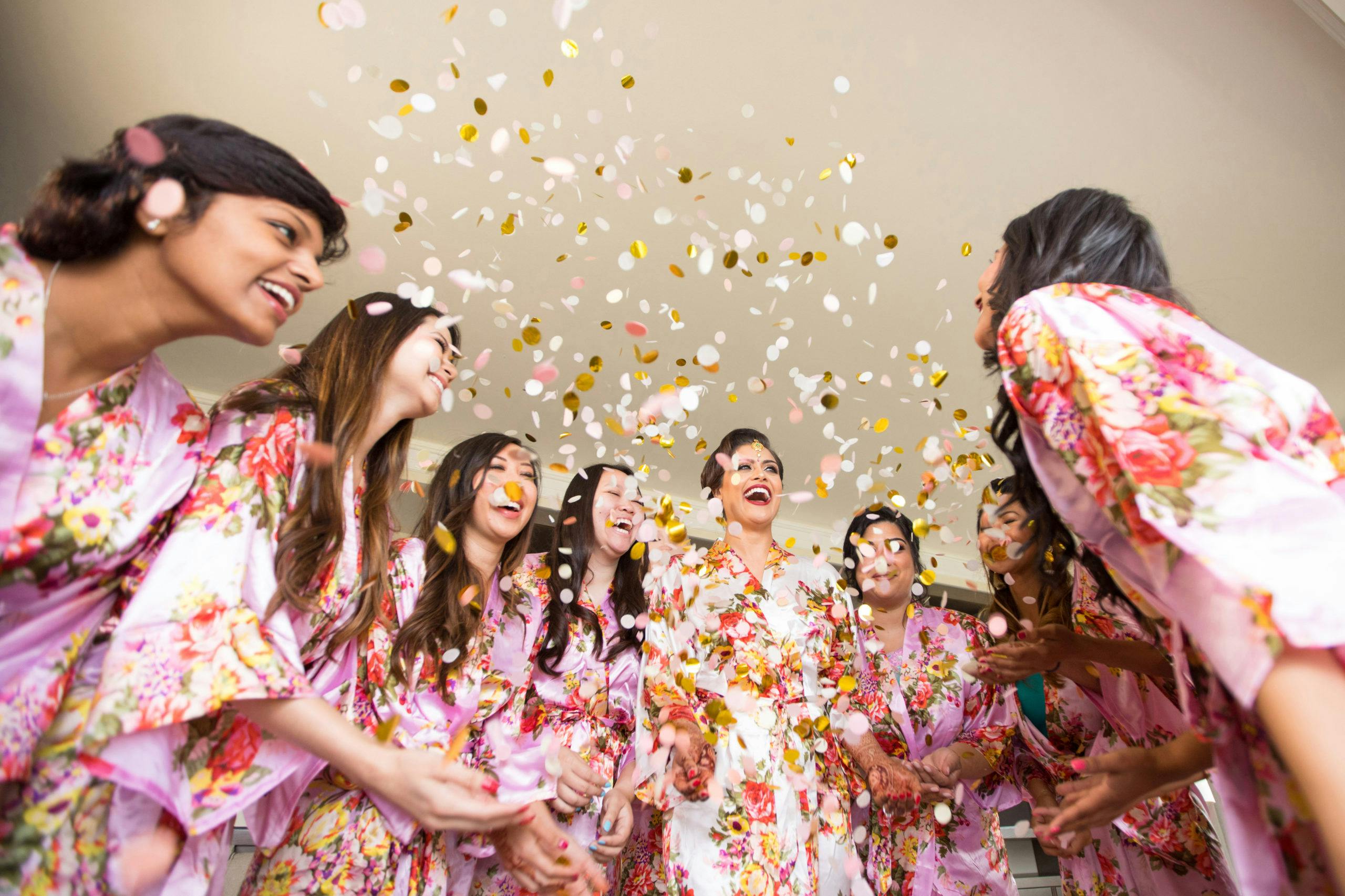 Bridesmaids huddled around in matching pajamas and confetti thrown in air | PartySlate
