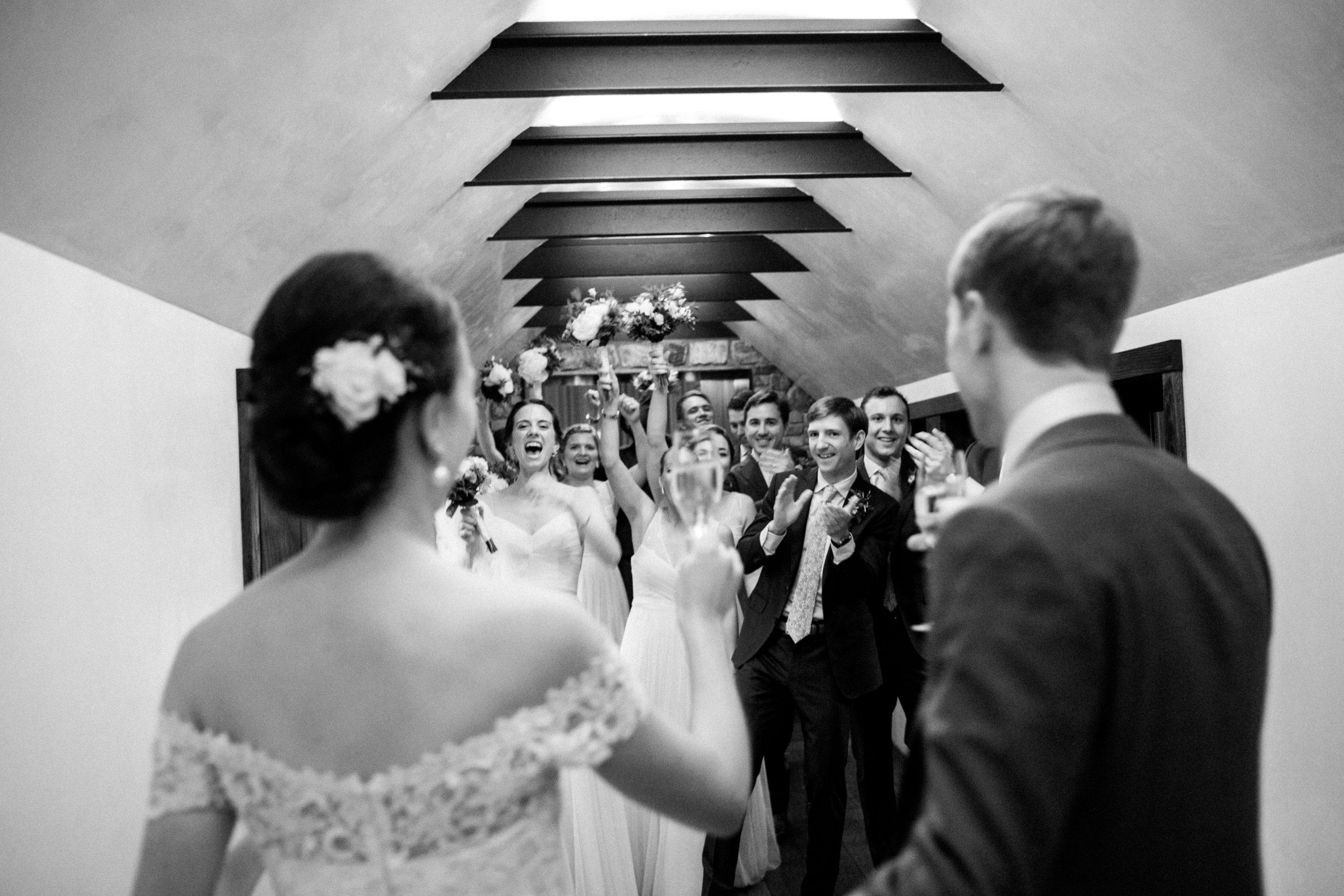 Black and white photo or bride and groom looking at cheering bridal party l PartySlate