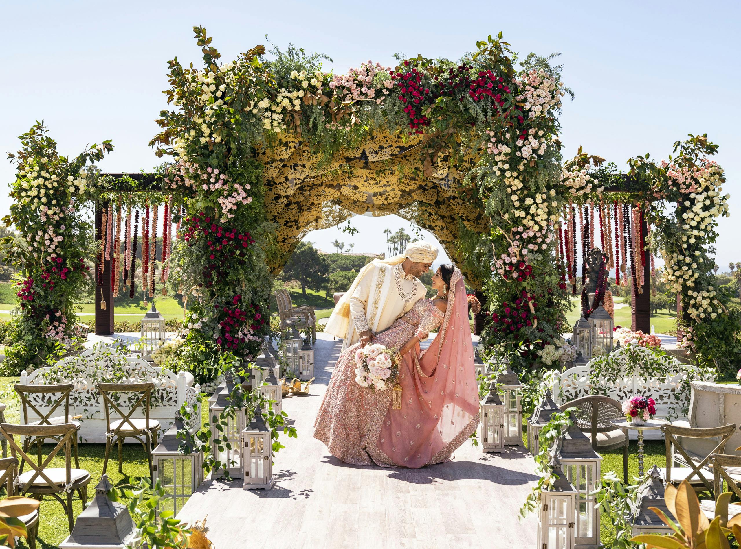 Groom dipping bride at traditional Indian wedding with colorful florals and greenery backdrop | PartySlate