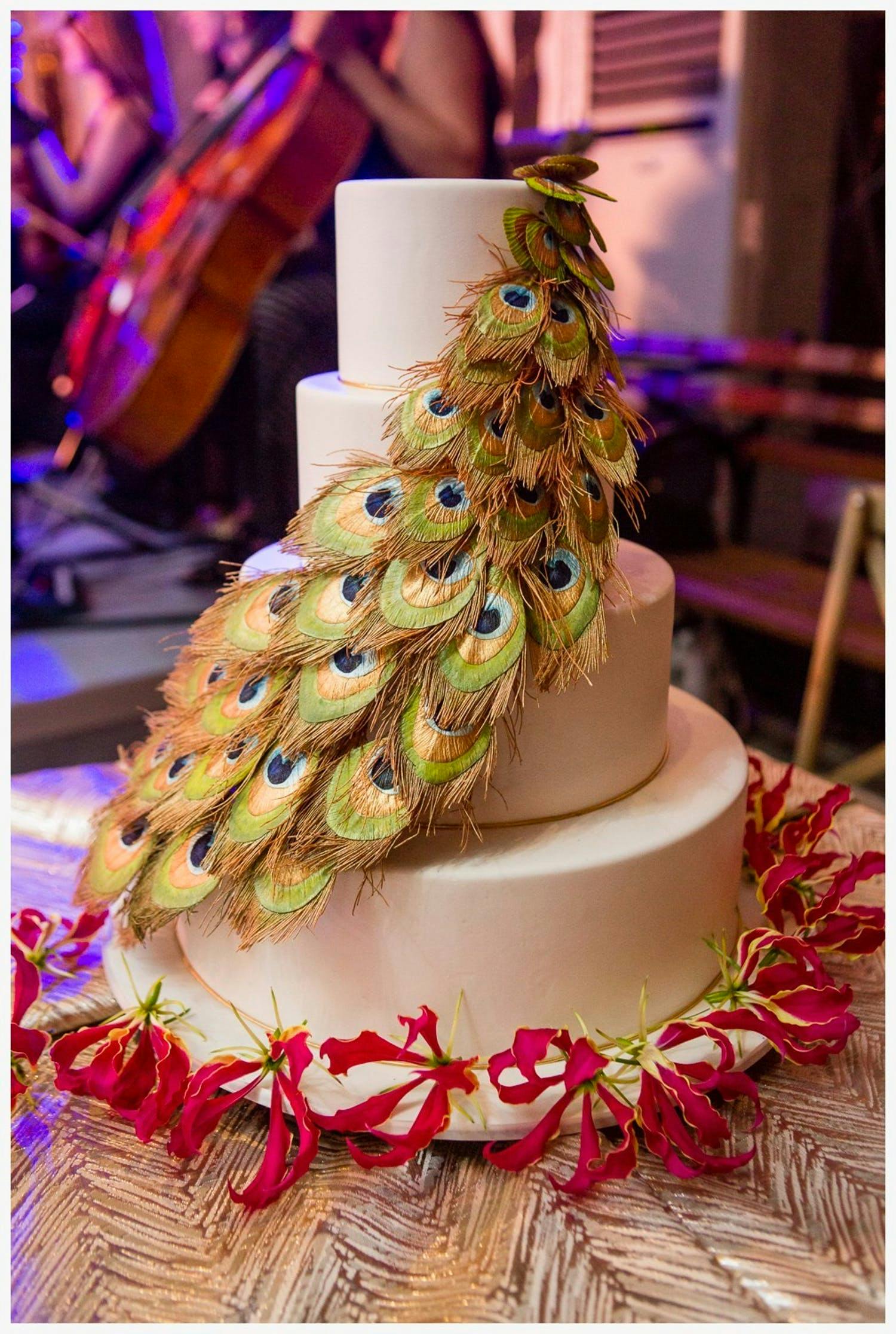 Three-tier white wedding cake with cascading peacock feathers | PartySlate