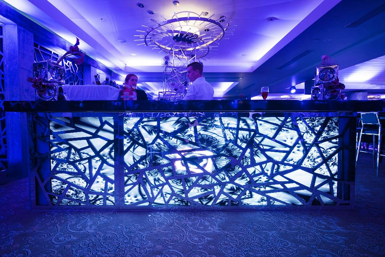 50th-birthday party with uplit ice-blue bar with geometric and fractured paneling in purple-uplit ballroom | PartySlate