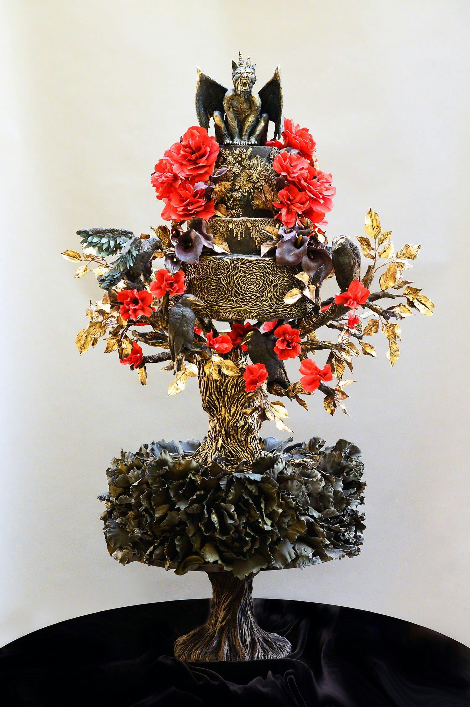 Unique black goth wedding cake with gargoyle topping and red and gold blooms | PartySlate