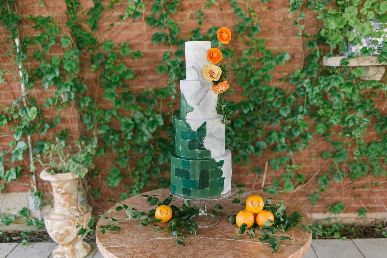 Four-tier circular wedding cake with mix of green tile designs and grey marble | PartySlate