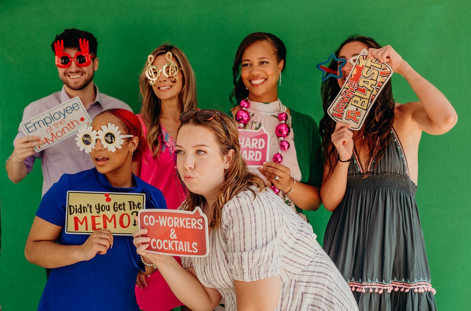 Guests pose against green backdrop at corporate event with fun photo props | PartySlate