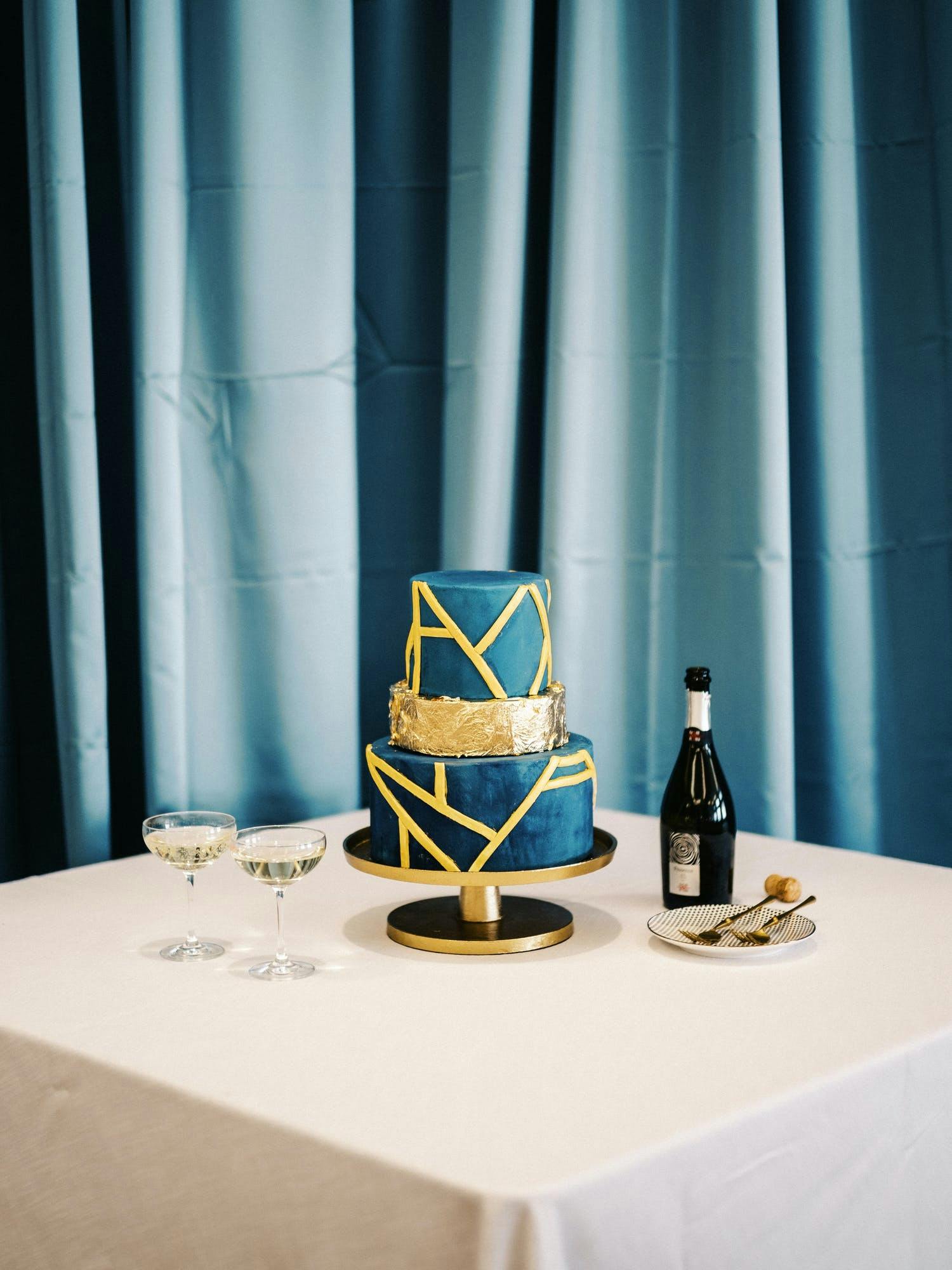 Three-tier blue and gold wedding cake with asymmetrical faceted shapes | PartySlate