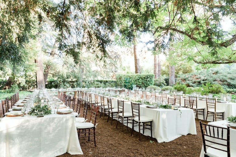 Wedding reception area in shaded winery garden with long white tables and wooden chairs at Beringer Winery | PartySlate
