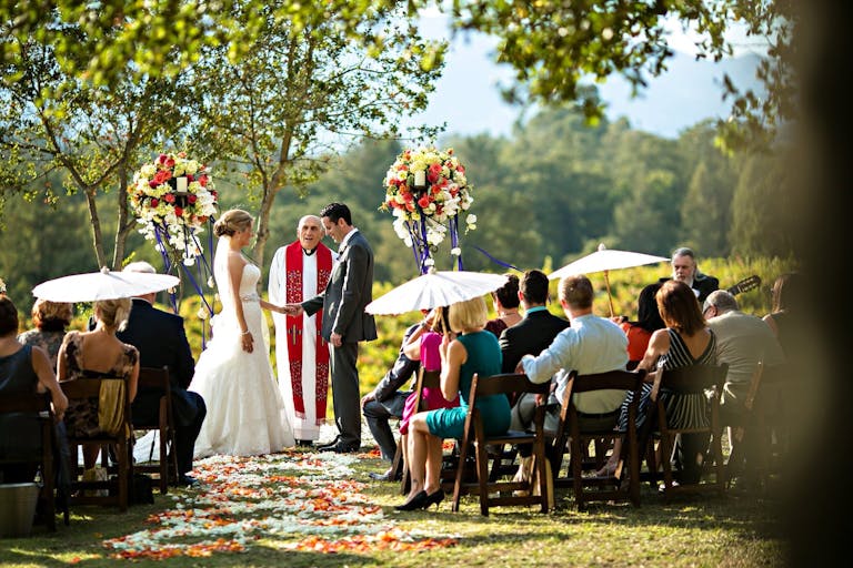 Couple exchanging vows at Sonoma winery ceremony decorated with bright floral arrangements and white umbrellas | PartySlate