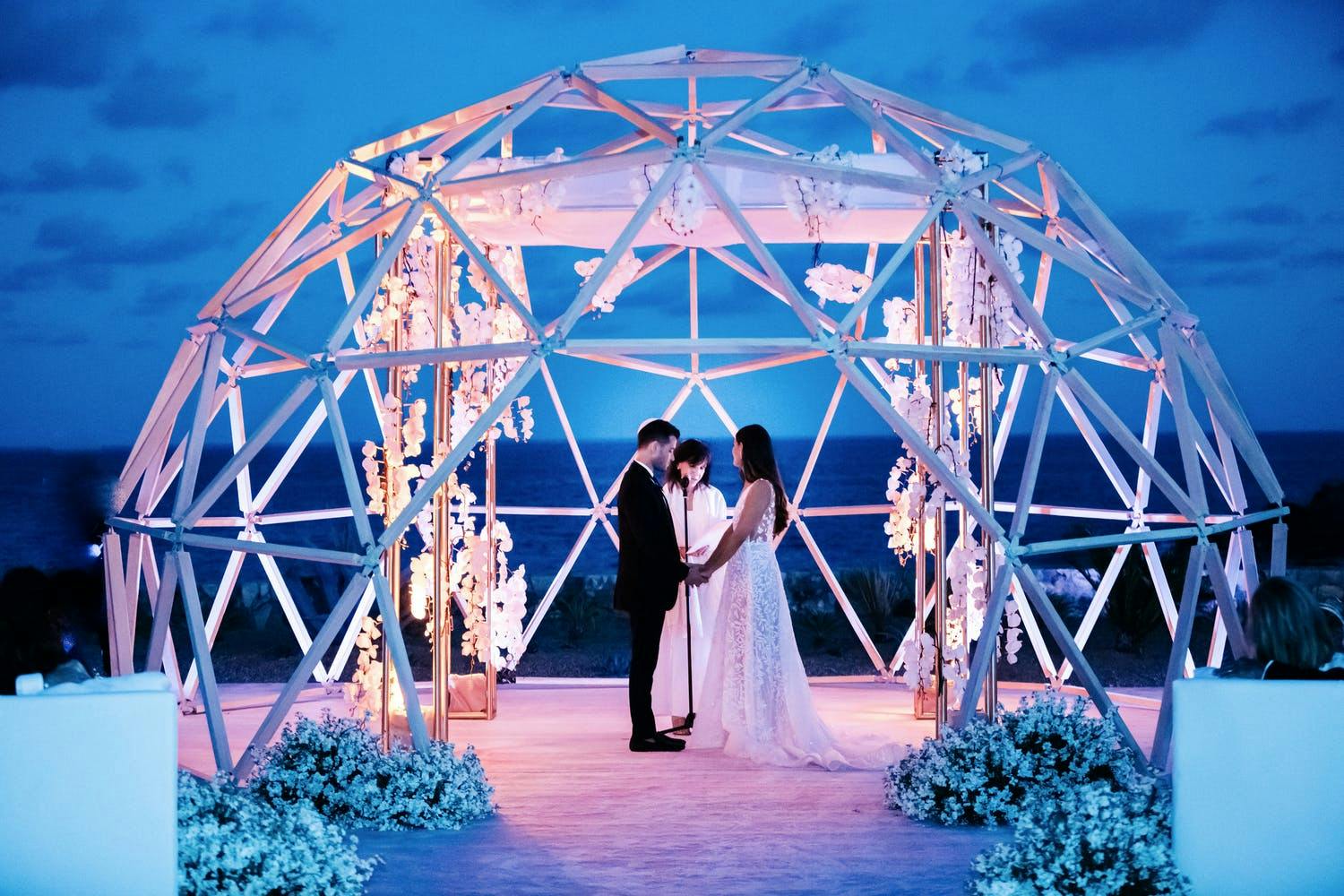 Couple exchange vows in a geometric wedding décor igloo-like structure | PartySlate