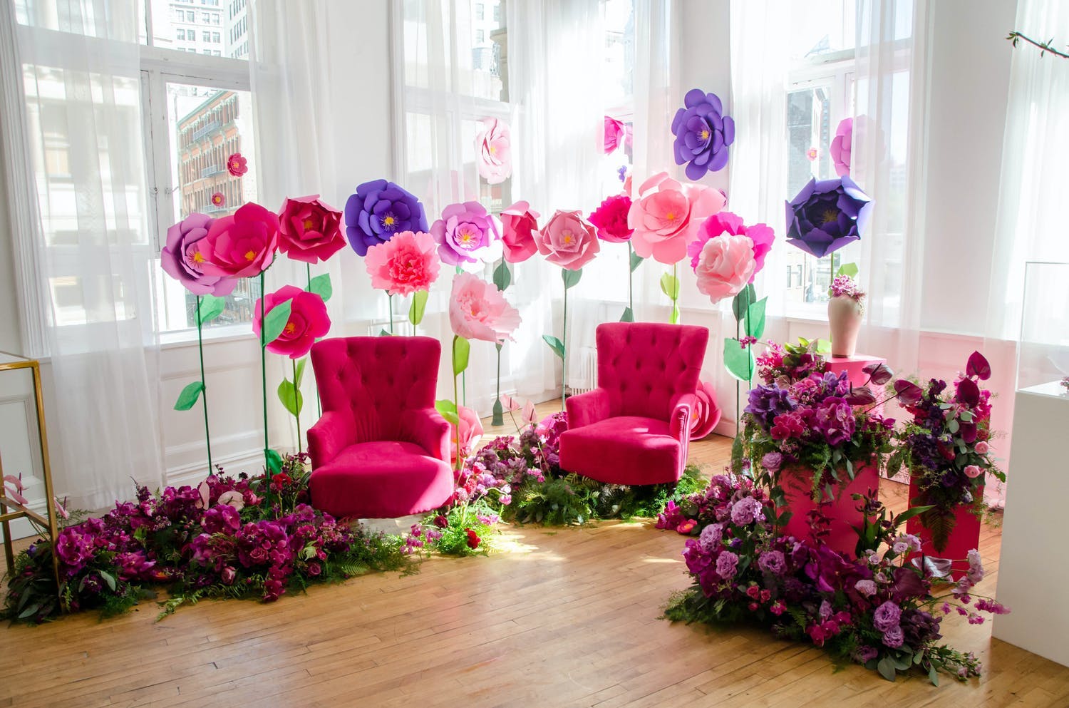 Media event with photo op area featuring two bright pink sofa chairs and giant pink, purple, and red paper flowers | PartySlate