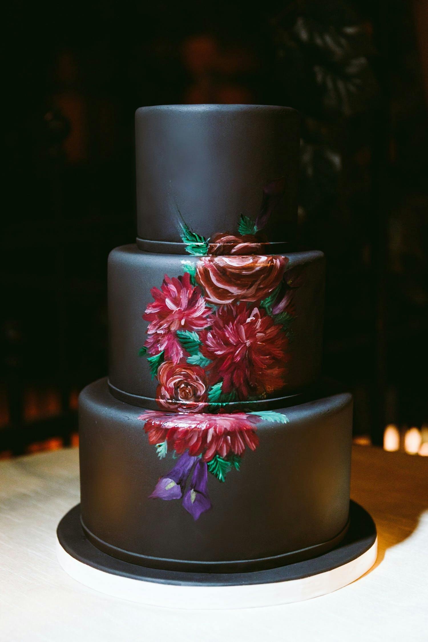 Three-tier black wedding cake with elegant rose design spanning across each tier | PartySlate