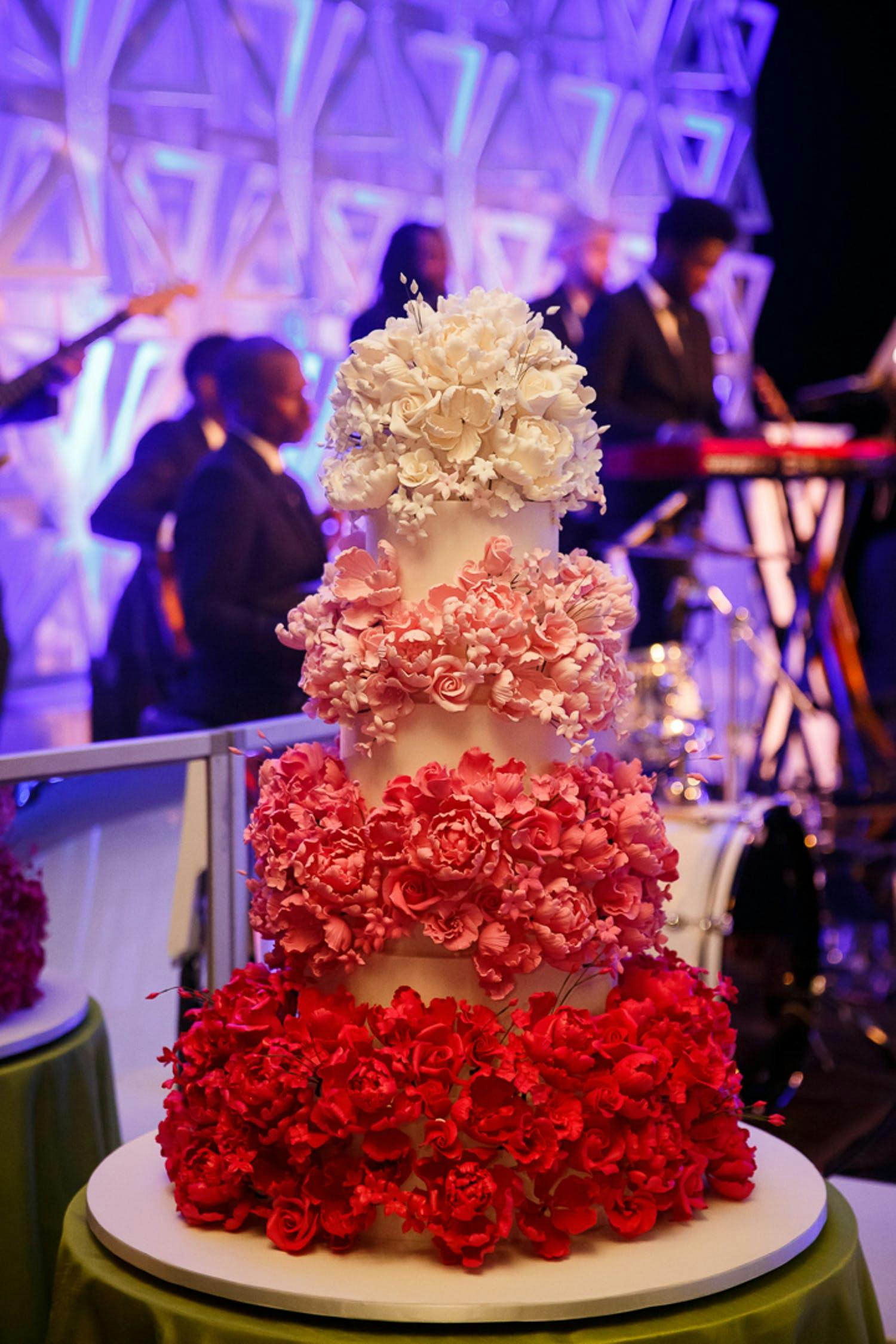Four-tier cake covered with ombré tiers of flowers going from red to dark pink to pink to white | PartySlate