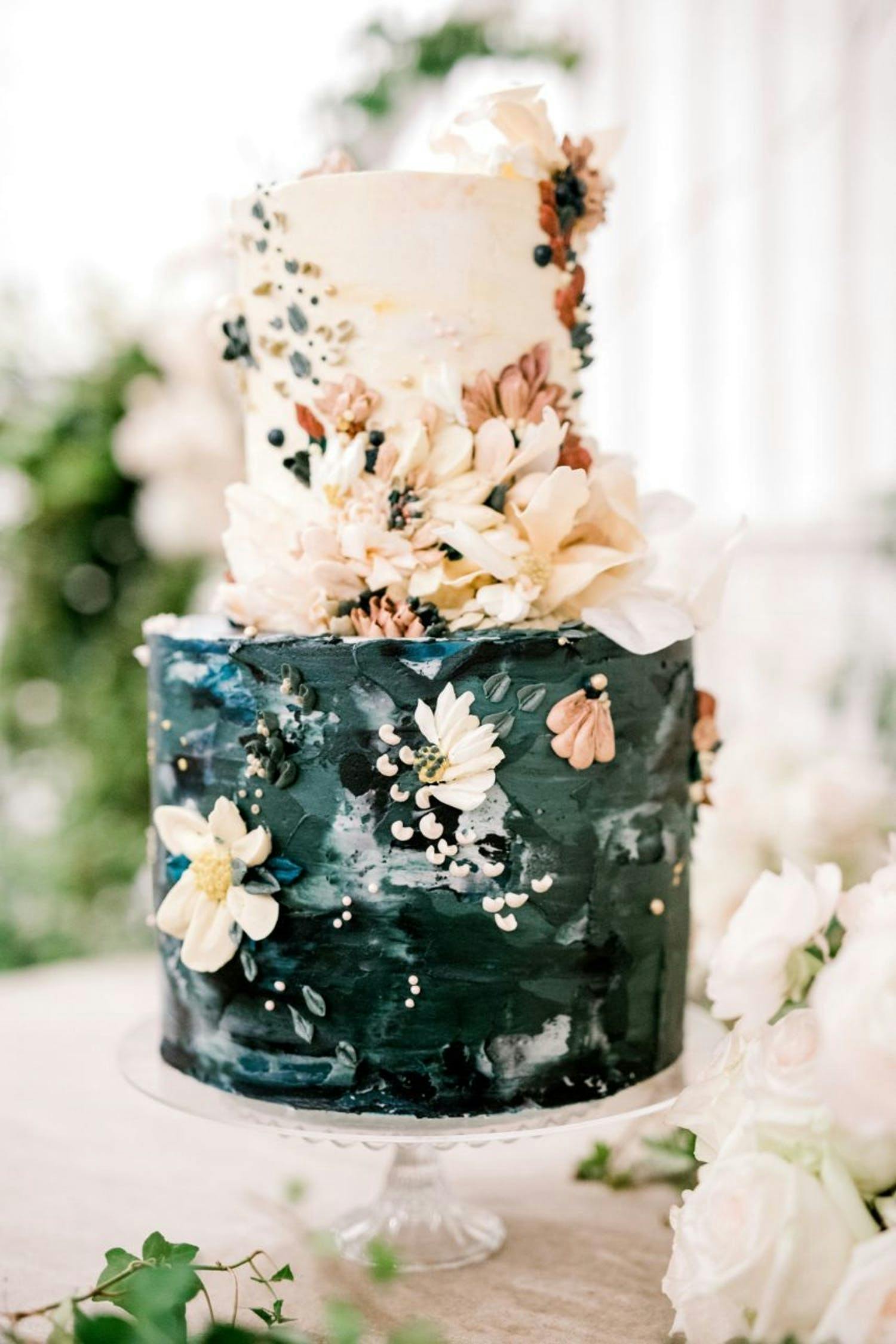 Two-tier wedding cake with green watercolor bottom and cream top with cream-hued flowers | PartySlate