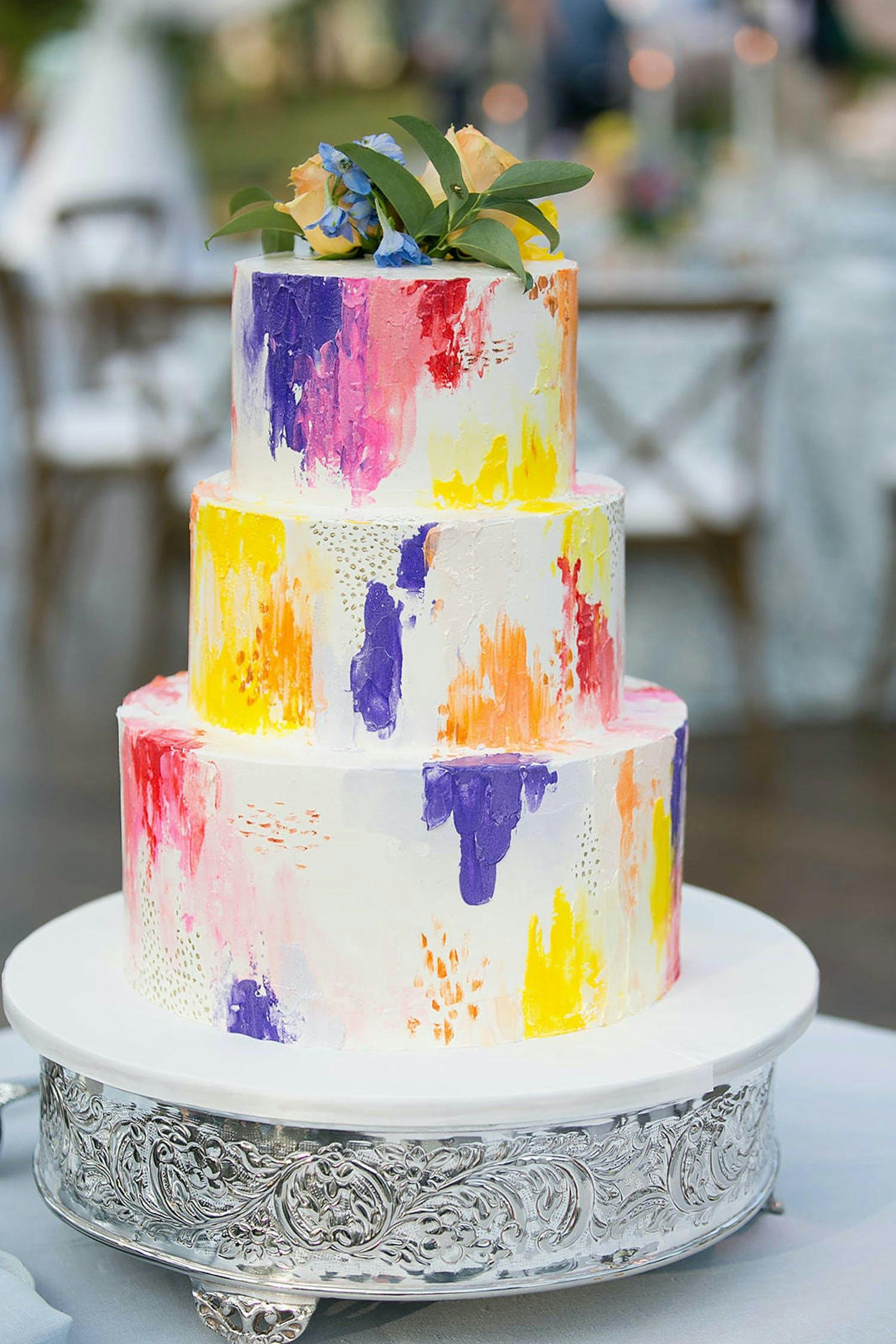 Three-tier white wedding cake with splatter of pink, purple, orange and yellow | PartySlate