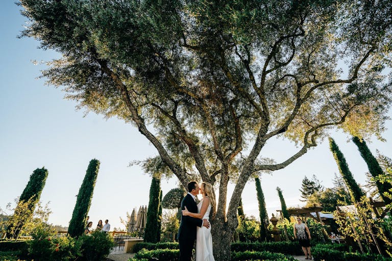 Bride and groom share a kiss in beautifully manicured garden at Regale Winery and Vineyards | PartySlate