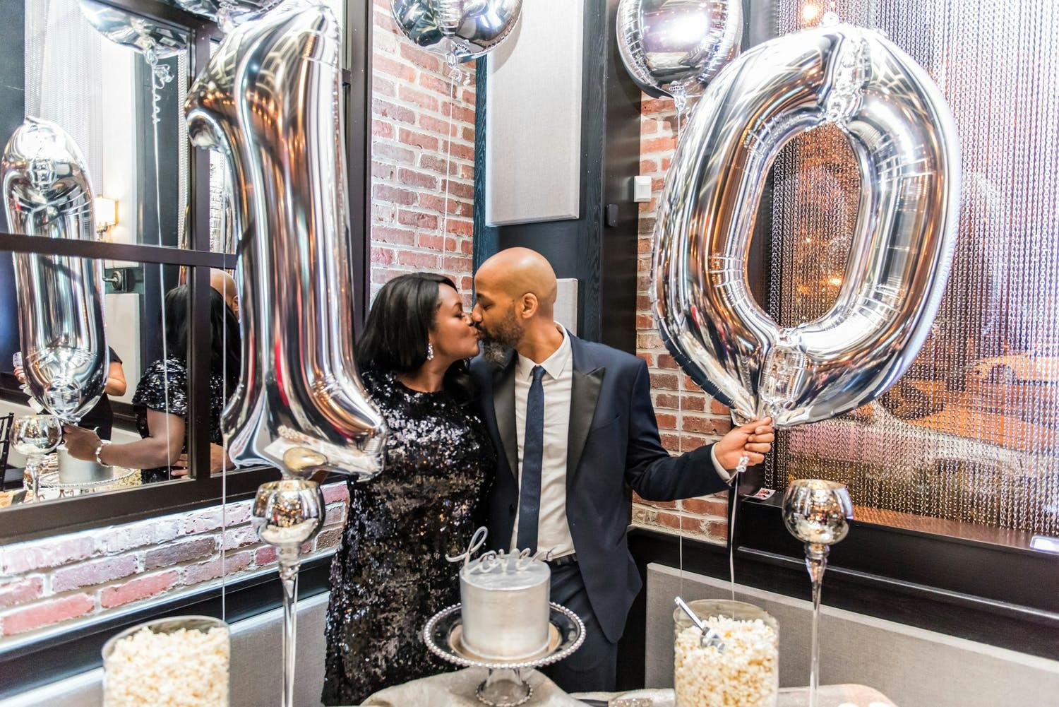 Couple kiss while holding silver balloons that spell out 10 for 10th-wedding anniversary party | PartySlate