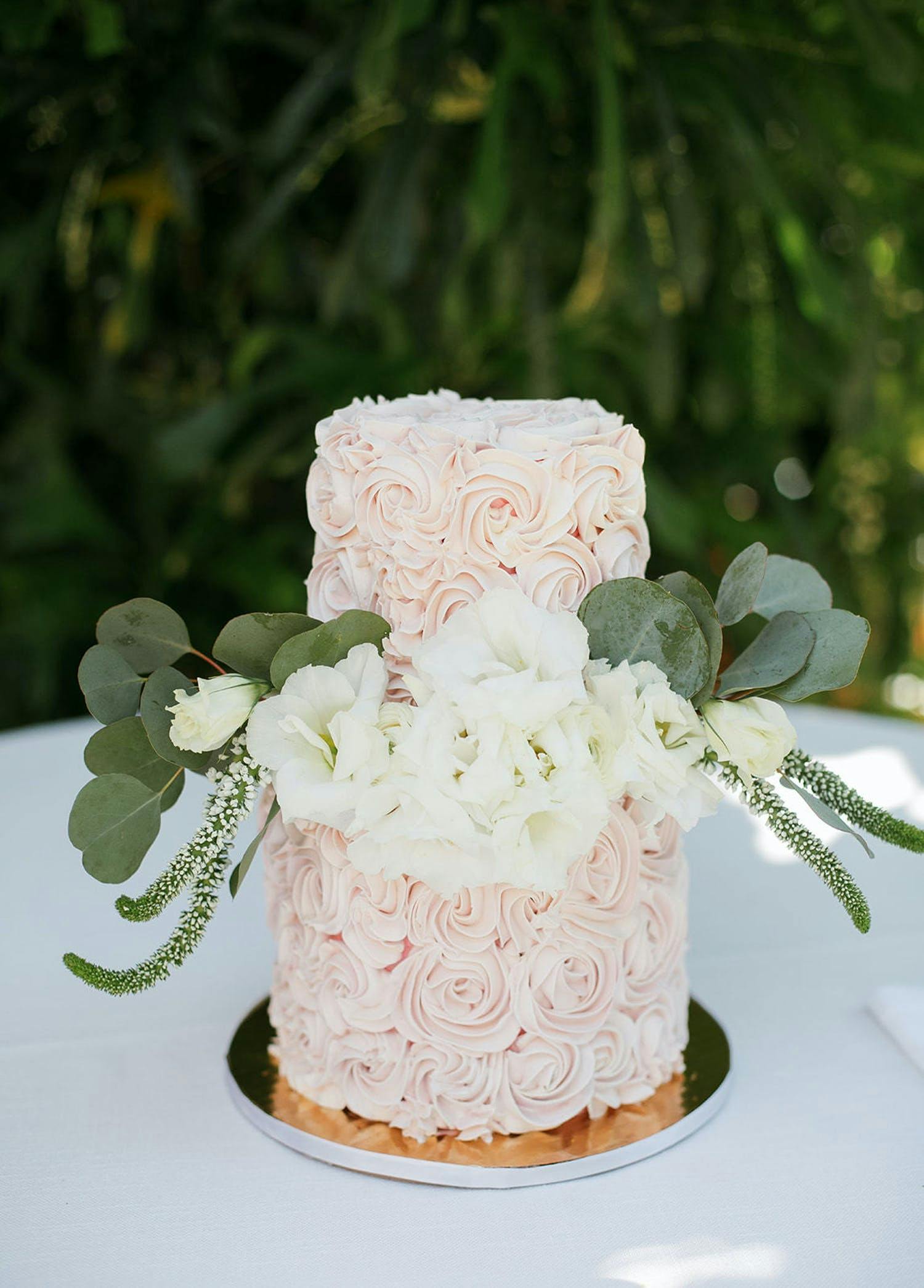 Pink buttercream cake with plush white florals and eucalyptus leaves between two tiers | PartySlate