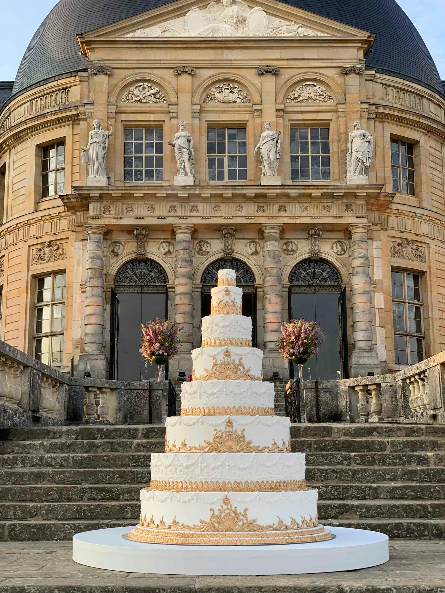 Towering eight tier white wedding cake with ornate gold icing designs | PartySlate