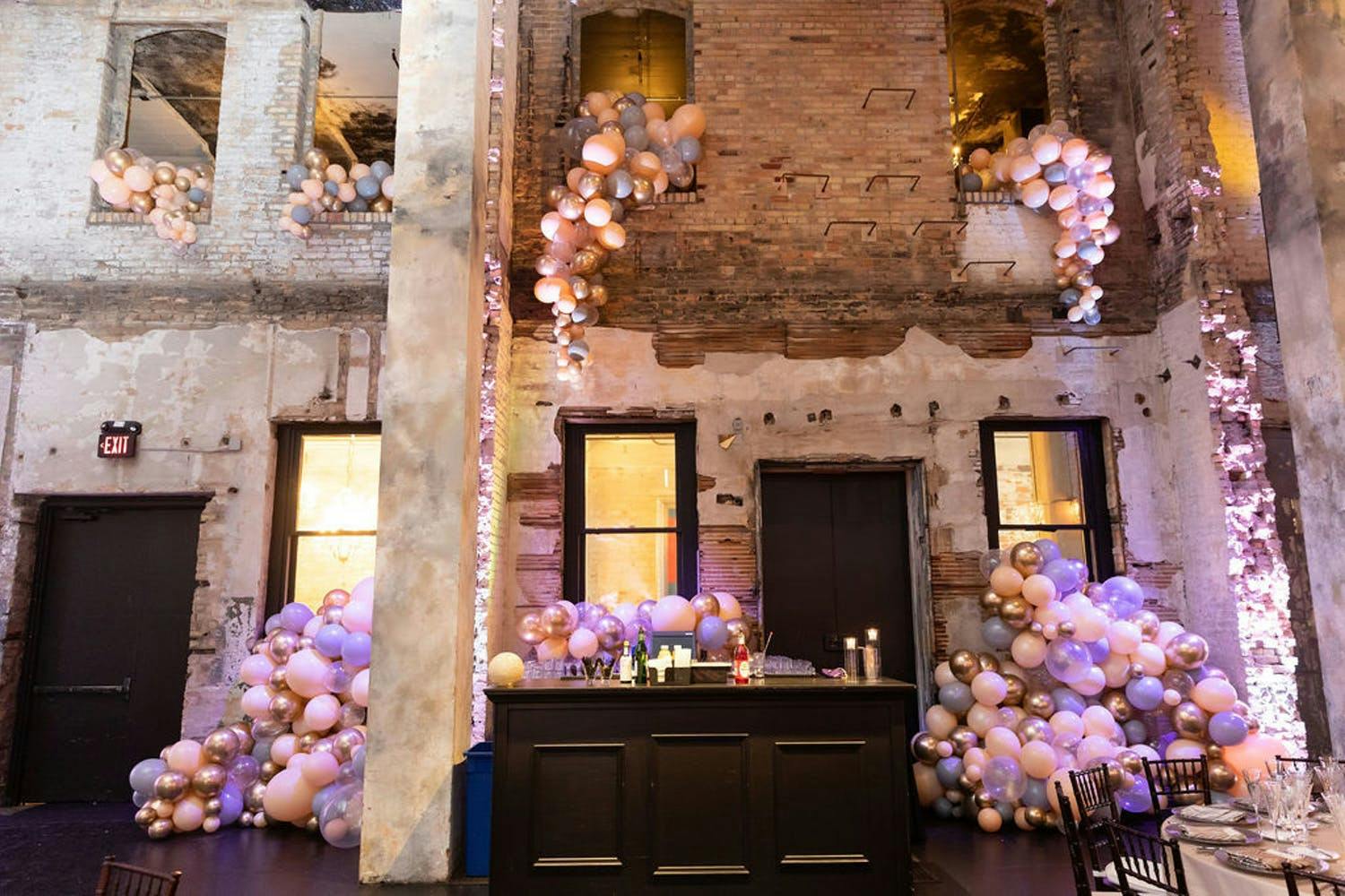 Raw Venue Space with Brick Soaring Walls Covered in Cascading Purple and Pink Balloons for 50th-Wedding Anniversary Party | PartySlate