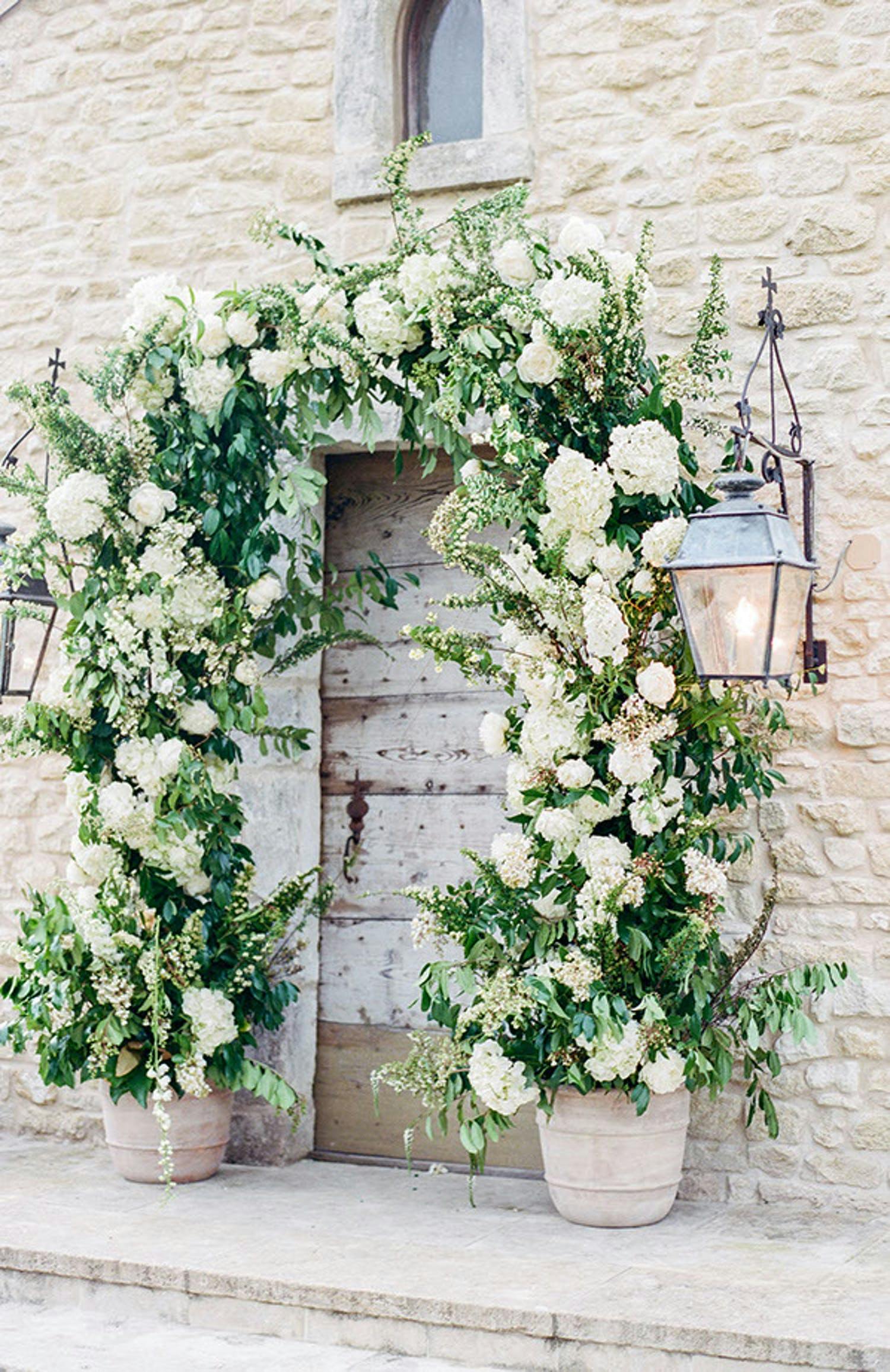 White and green floral arch over outside door at white country wedding designed by Events in Bloom | PartySlate