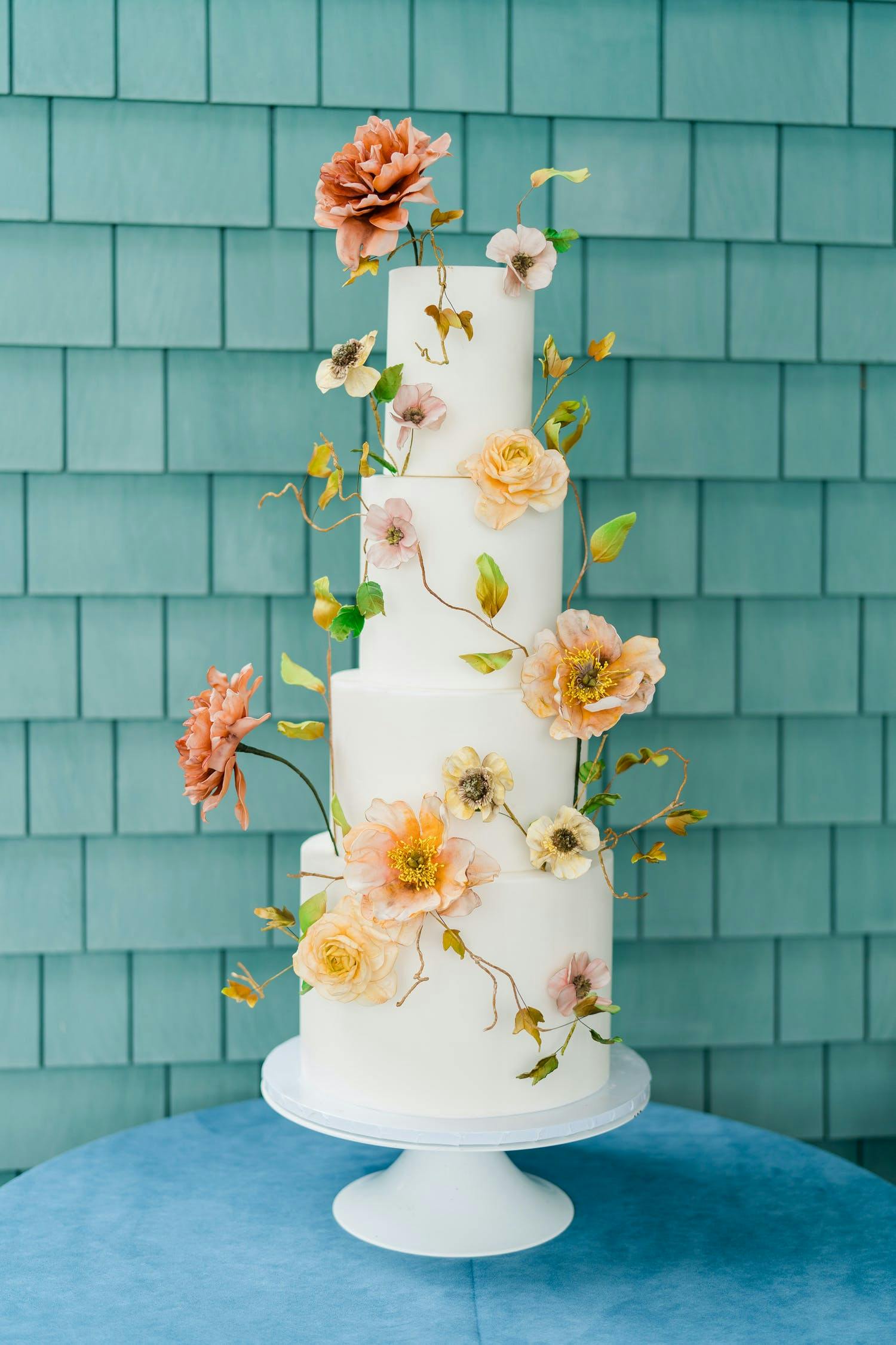 Simple and four-tier white wedding cake decorated with both flowers and stems | PartySlate