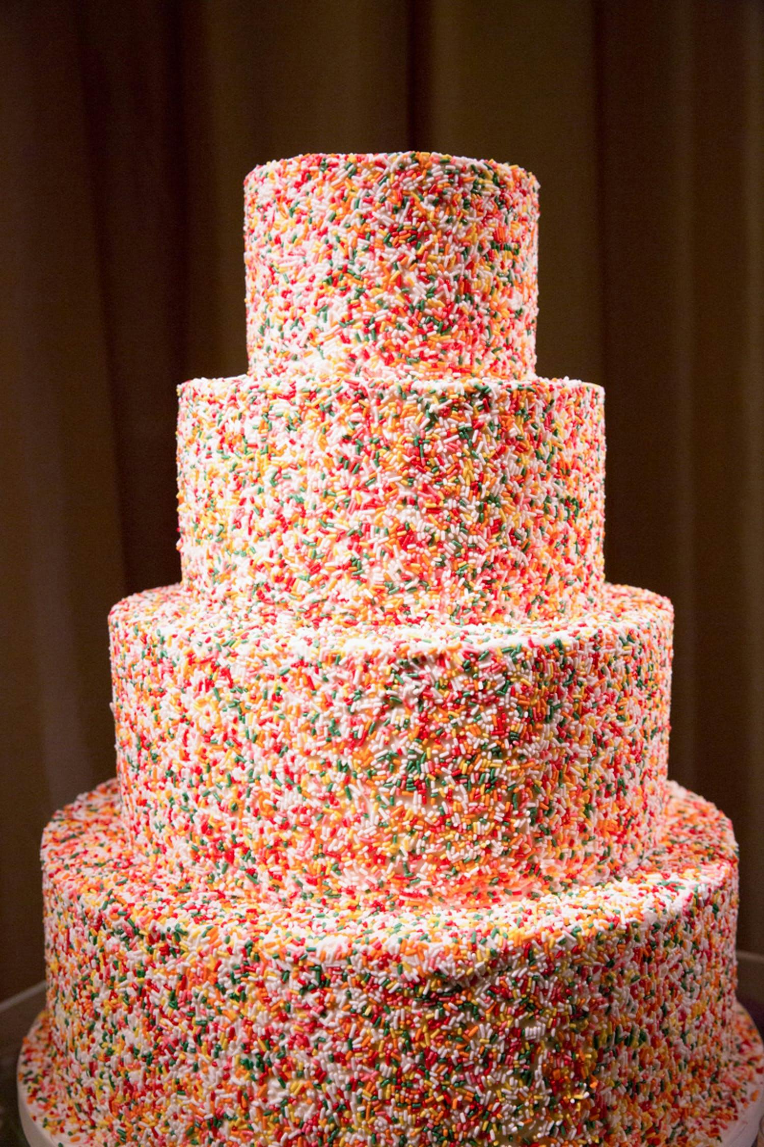 Large four-tier wedding cake covered in colorful sprinkles | PartySlate