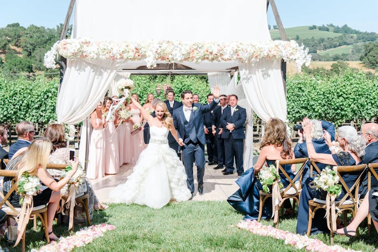 Newlyweds rejoice at the altar as loved ones cheer and photograph at beautiful outdoor wedding at deLorimier Winery in Geyserville, CA | PartySlate