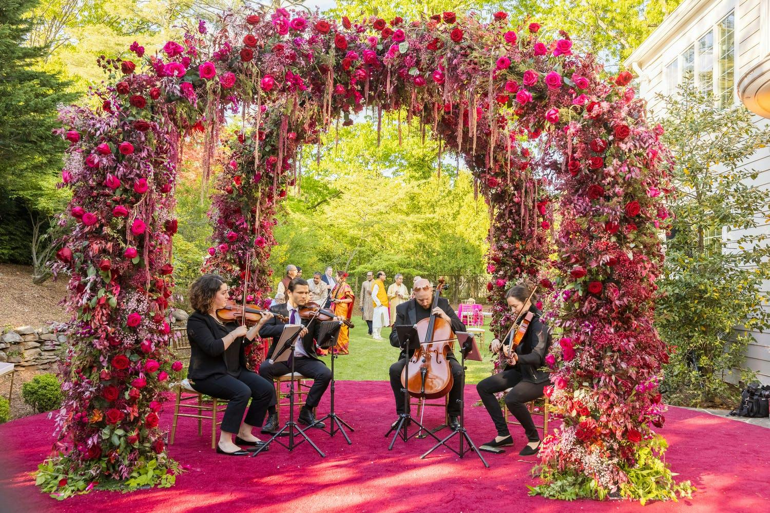 String quartet plays under double arch of bright pink blooms for wedding cocktail hour | PartySlate