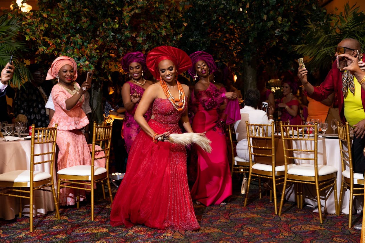 Bride dances in red dress and gele before her female relatives at a Nigerian wedding | PartySlate