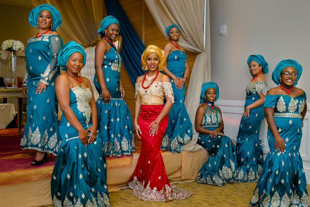 Bride in red and gold wedding attire poses with maidens in blue aso-ebi at Nigerian wedding | PartySlate
