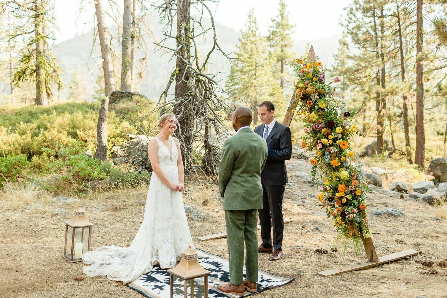 intimate micro wedding ceremony in woods with triangle arch with one side covered in flowers | PartySlate