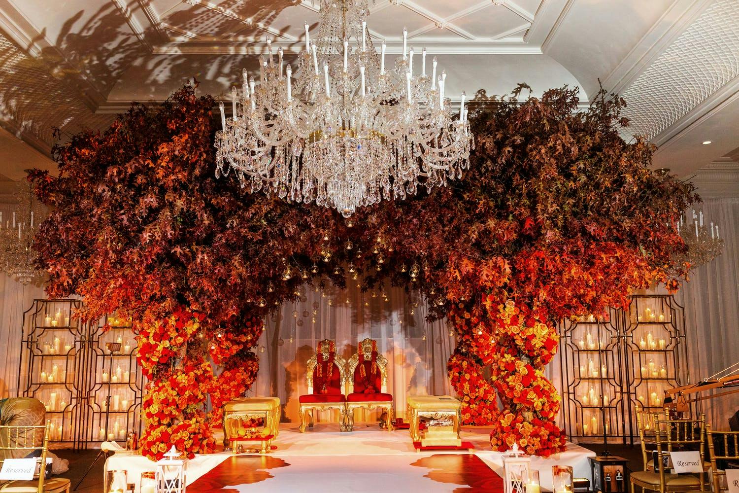 Fall wedding mandap with red and orange flower pillars and crown of autumn leaves | PartySlate