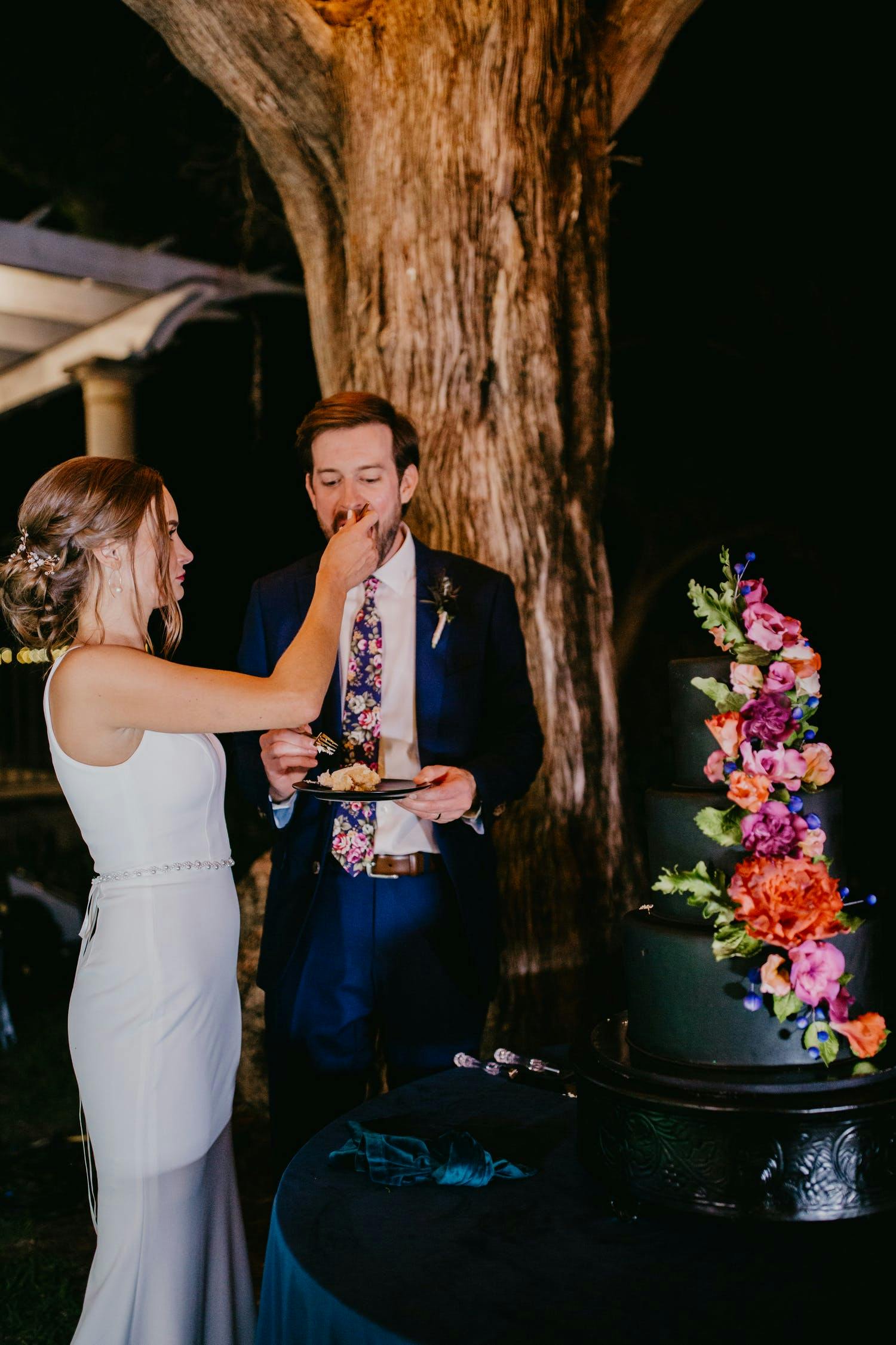 Bride and groom cut black wedding cake with colorful flowers at evening outdoor small wedding | PartySlate