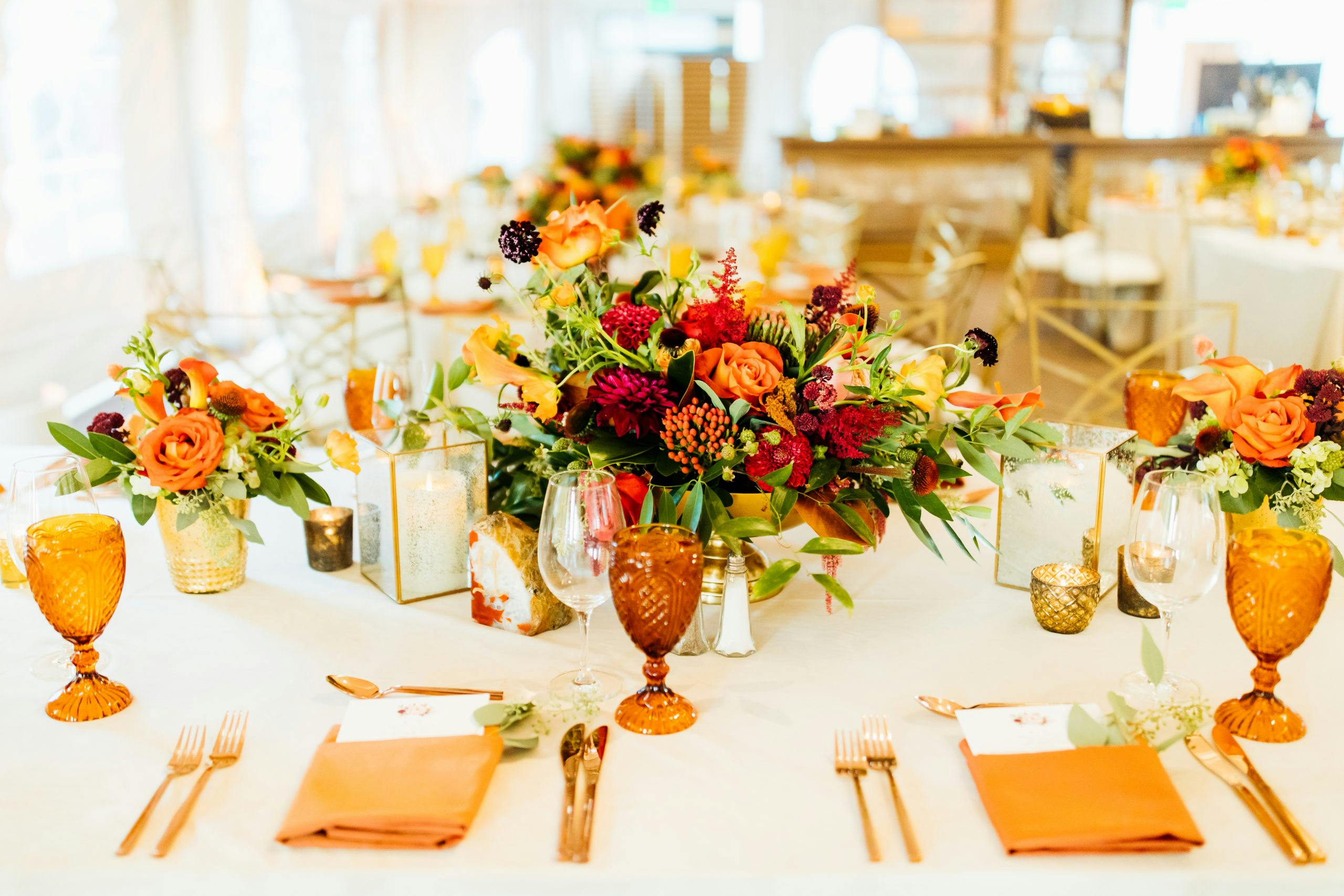A fall wedding reception table with amber glassware that matches the burnt orange floral centerpieces | PartySlate