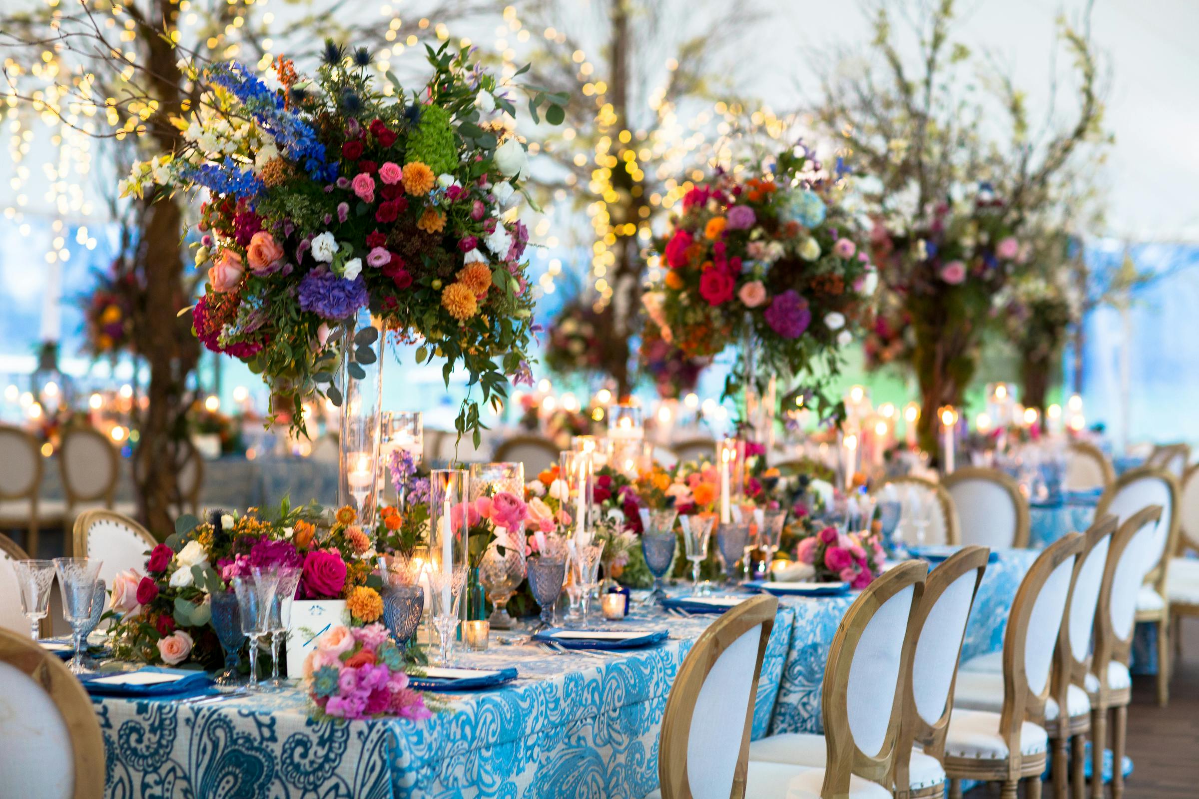 A long wedding tablescape filled with tall colorful floral centerpieces and shorter candles | PartySlate