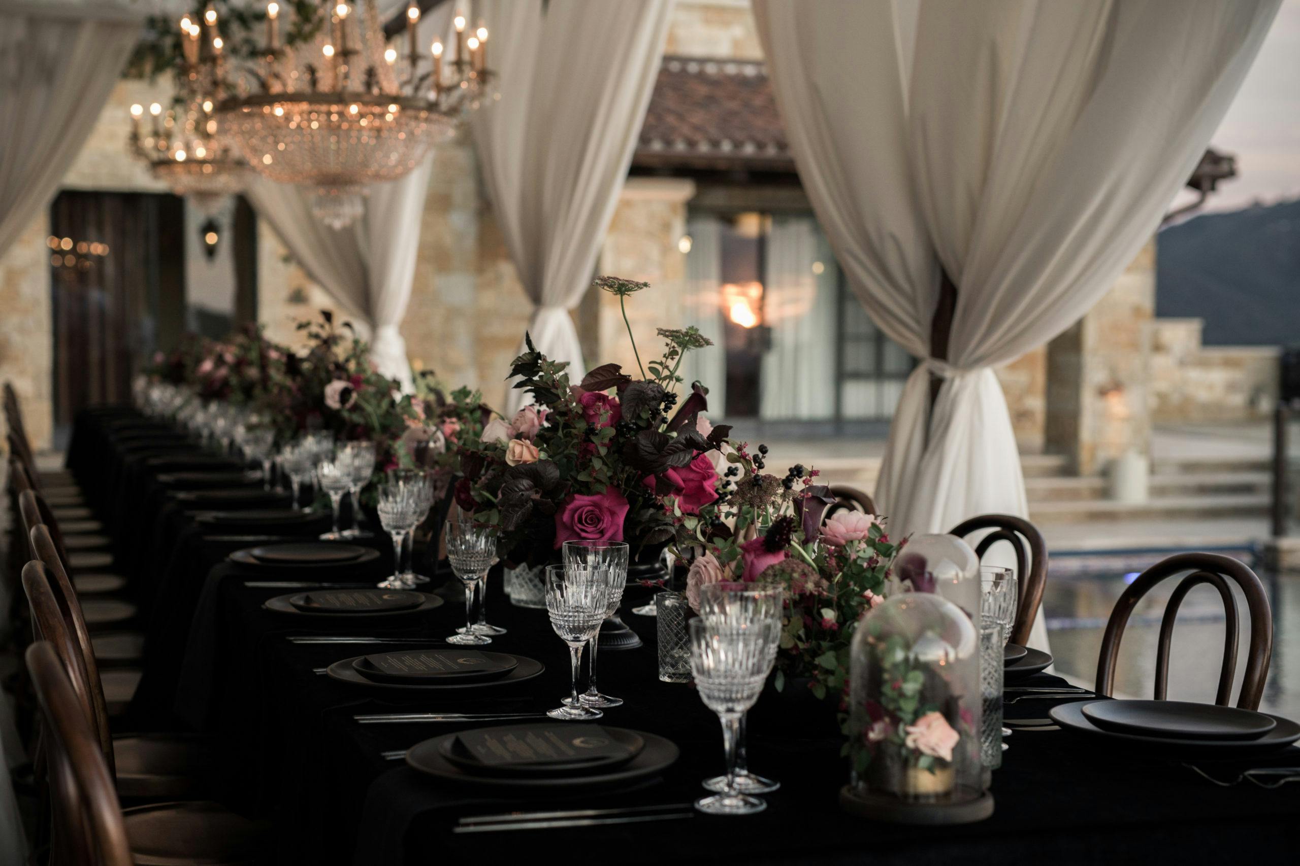 An all black table setting with dark-hued floral centerpieces at an autumn wedding | PartySlate