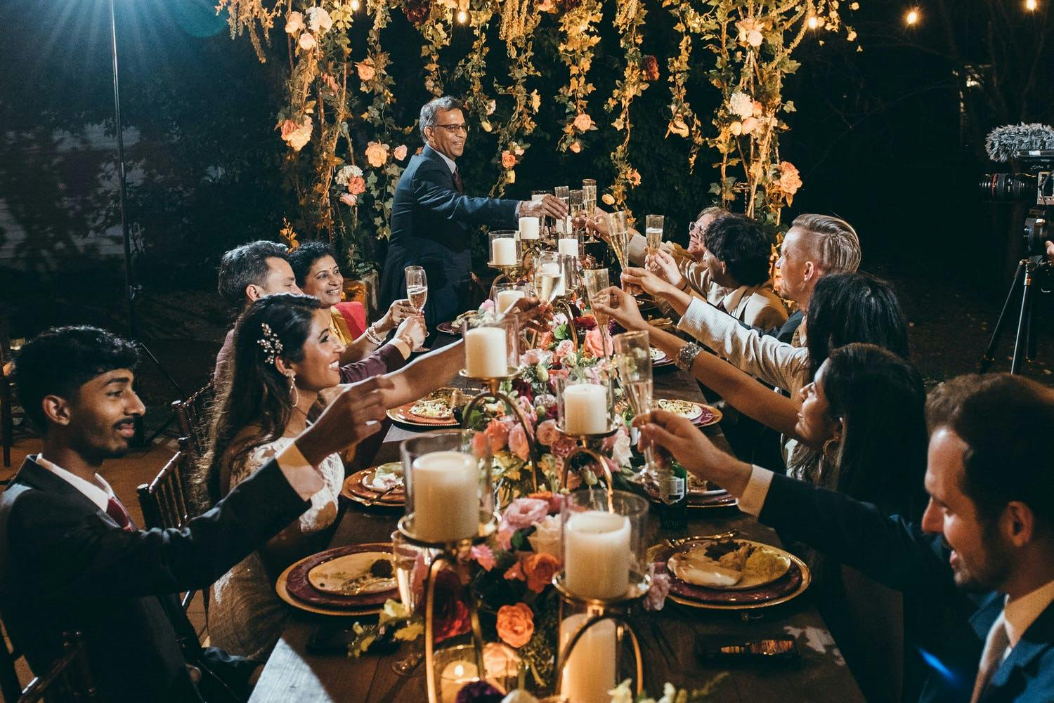 Night time wedding reception with king's table laden in candlelight and a floral installation at one end | PartySlate