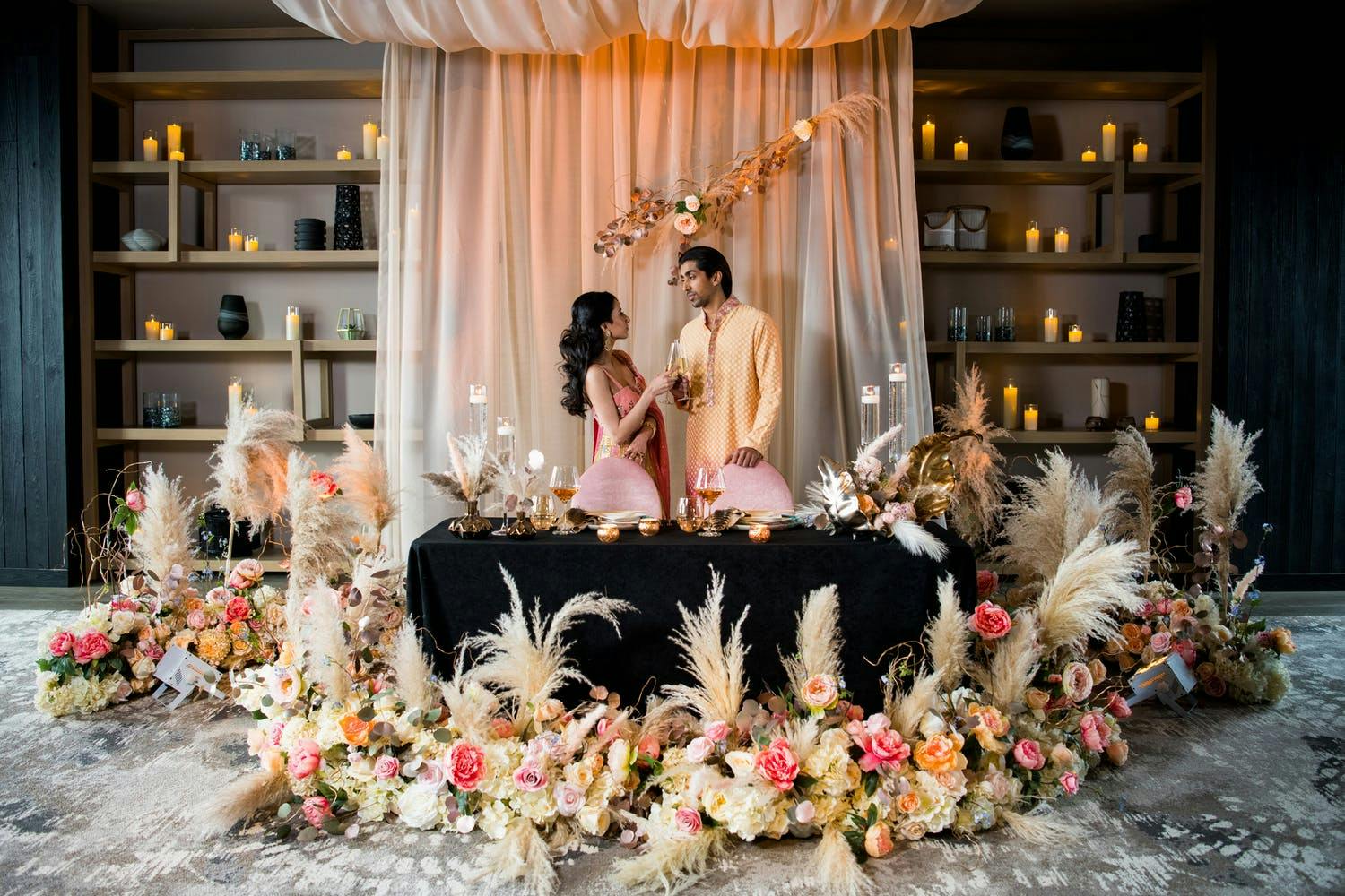 Modern South Asian wedding with black sweetheart table, dreamy pink drapery backdrop, and boho floral décor with pampas grass | PartySlate