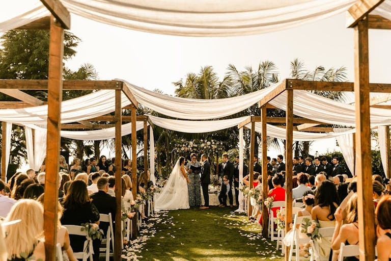 Wedding Draped with White Cloth Over Pergolas Lining The Aisle | ParrtySlate