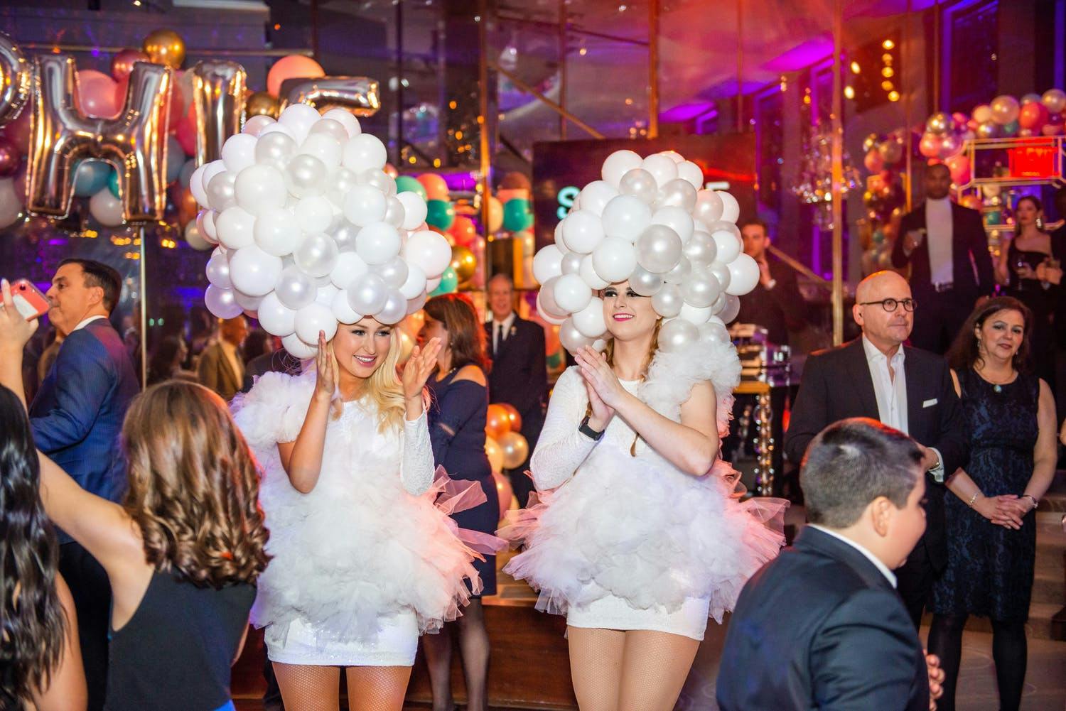 Two women wear white balloon headdresses at Bat Mitzvah filled with lavish balloon décor | PartySlate